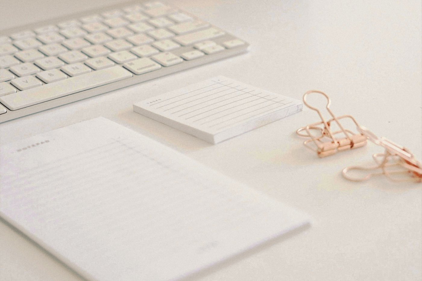 Escritorio blanco con teclado, bloc de notas y clips de cobre